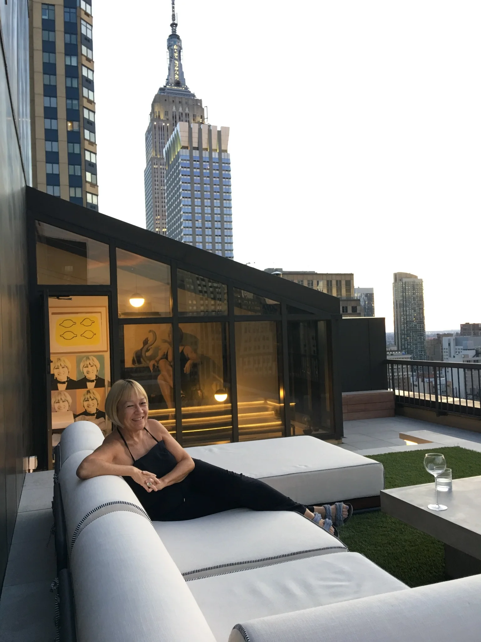 Cindy Gallop reclining on a white terrace sofa, with the Empire State Building visible behind her.